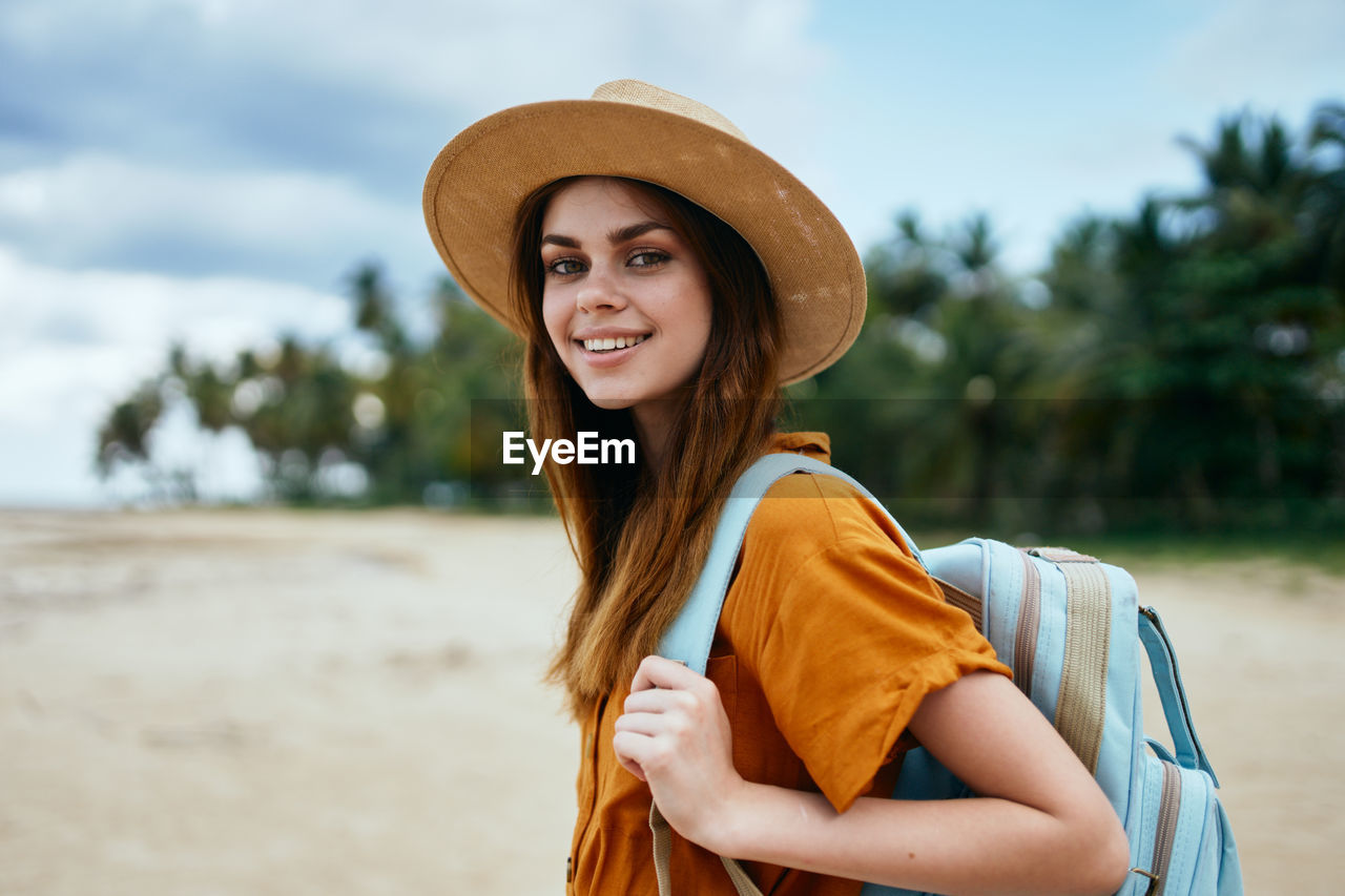 PORTRAIT OF SMILING YOUNG WOMAN WEARING HAT STANDING ON LAND