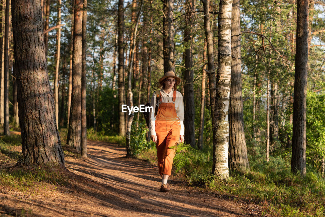 Woman botanist with backpack on ecological hiking trail in forest. naturalist exploring wildlife