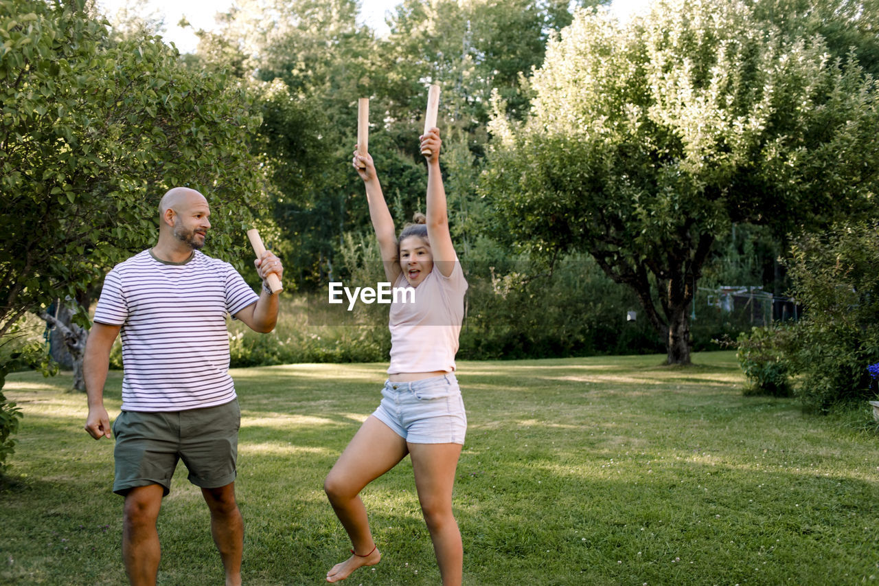 Father looking at daughter with hand raised while playing molkky in yard