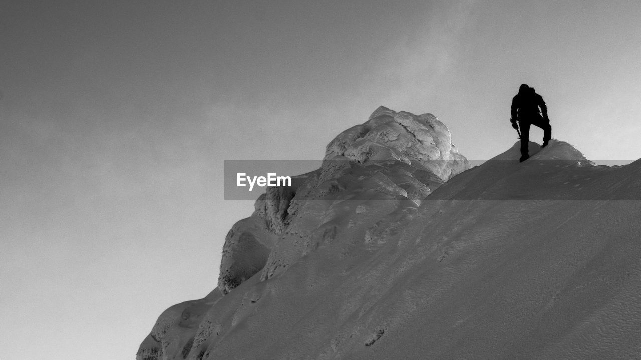 LOW ANGLE VIEW OF SILHOUETTE MAN AGAINST SNOWCAPPED MOUNTAIN