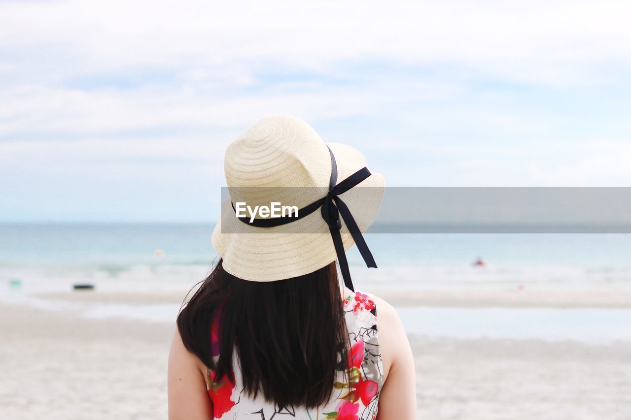 Rear view of woman wearing hat at beach against sky