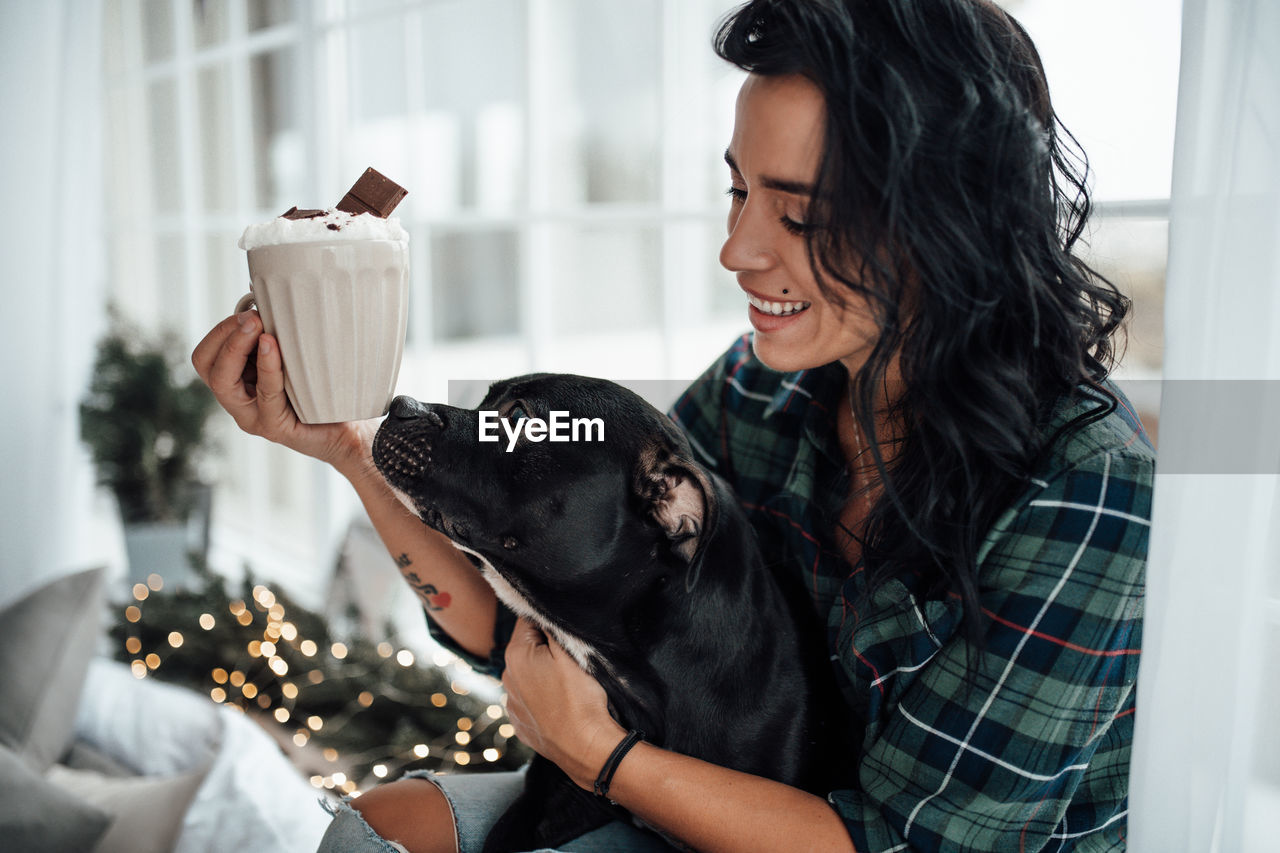 Smiling woman holding hot chocolate while sitting with dog at home