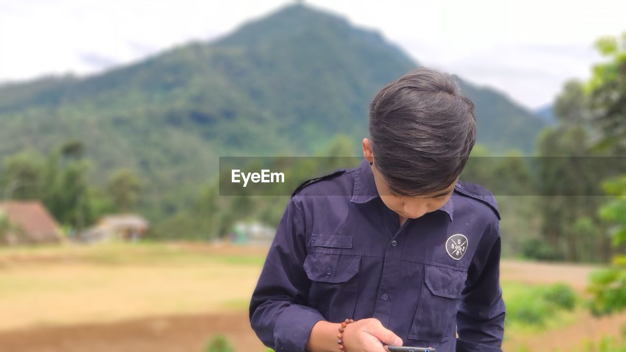 MAN STANDING ON FIELD AGAINST MOUNTAINS