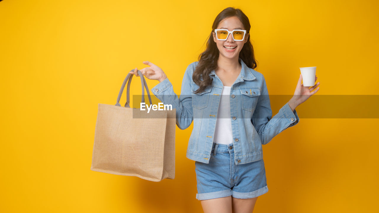 PORTRAIT OF SMILING YOUNG WOMAN AGAINST YELLOW WALL