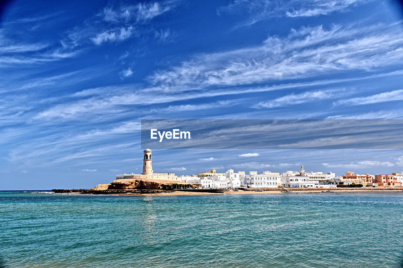 Lighthouse by sea against buildings in city