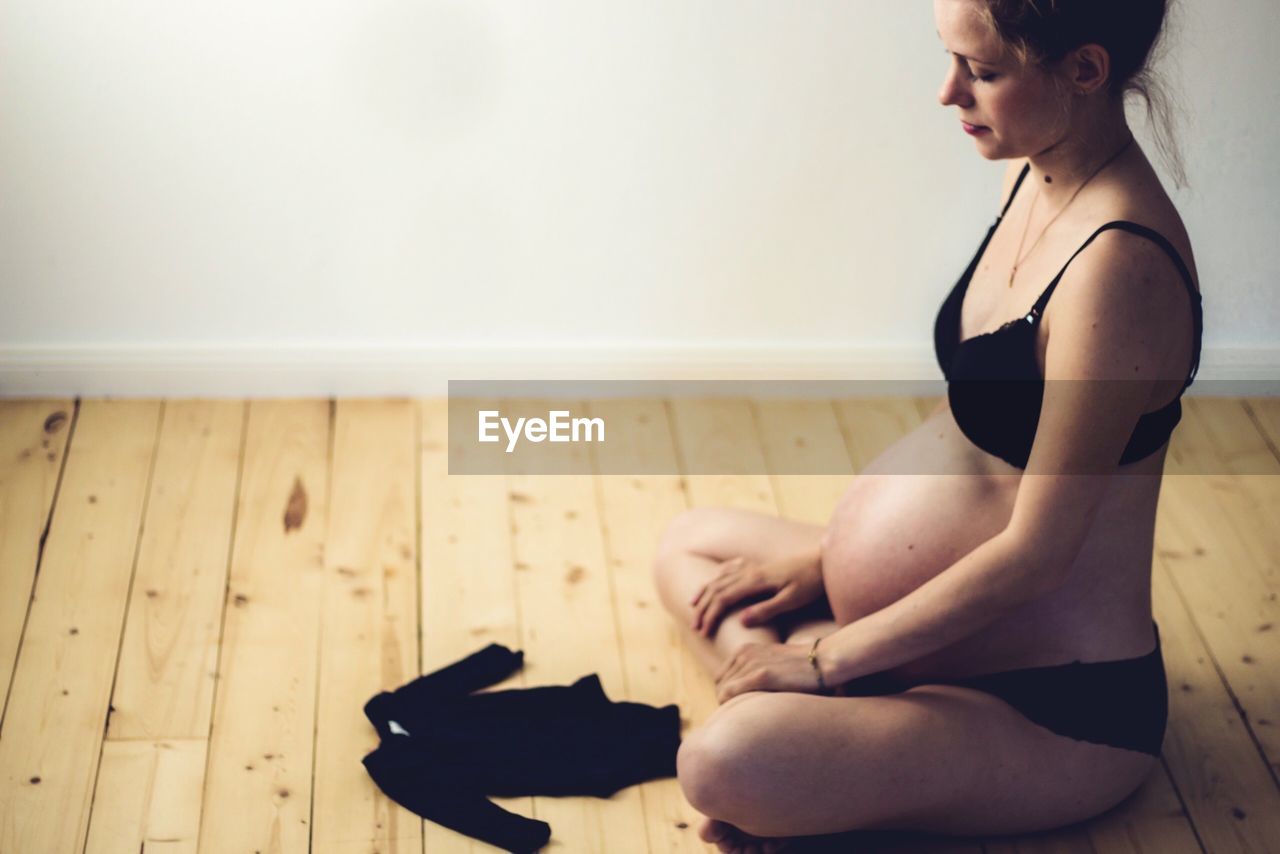 Pregnant woman with baby clothing sitting on hardwood floor