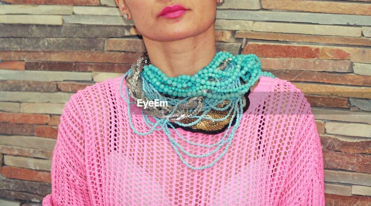 Midsection of woman wearing necklaces against wall