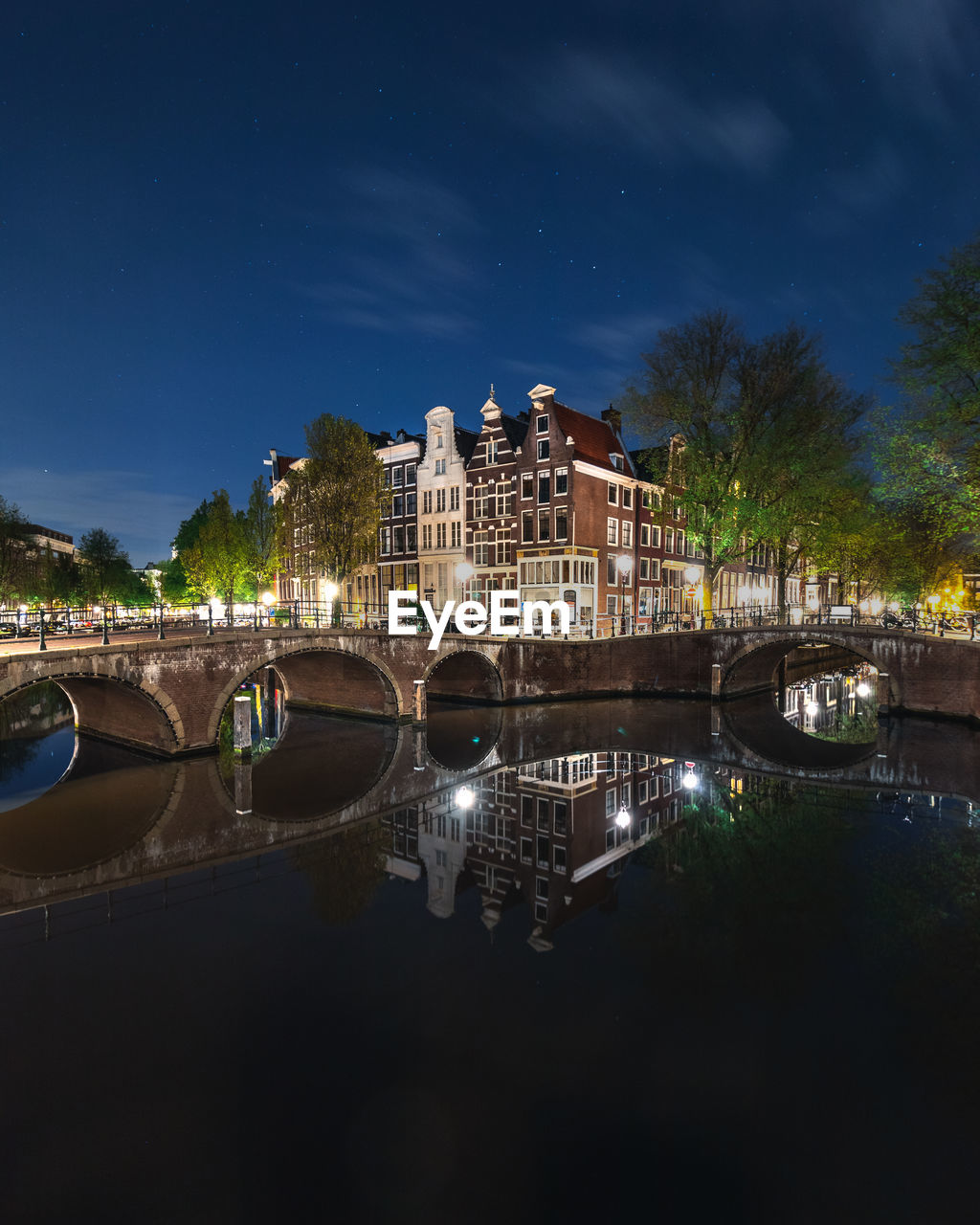 Bridge over river by illuminated buildings against sky at night in amsterdam, netherlands