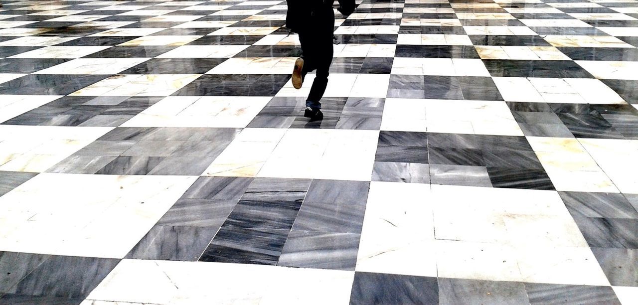 Low section of man running on chess patterned floor