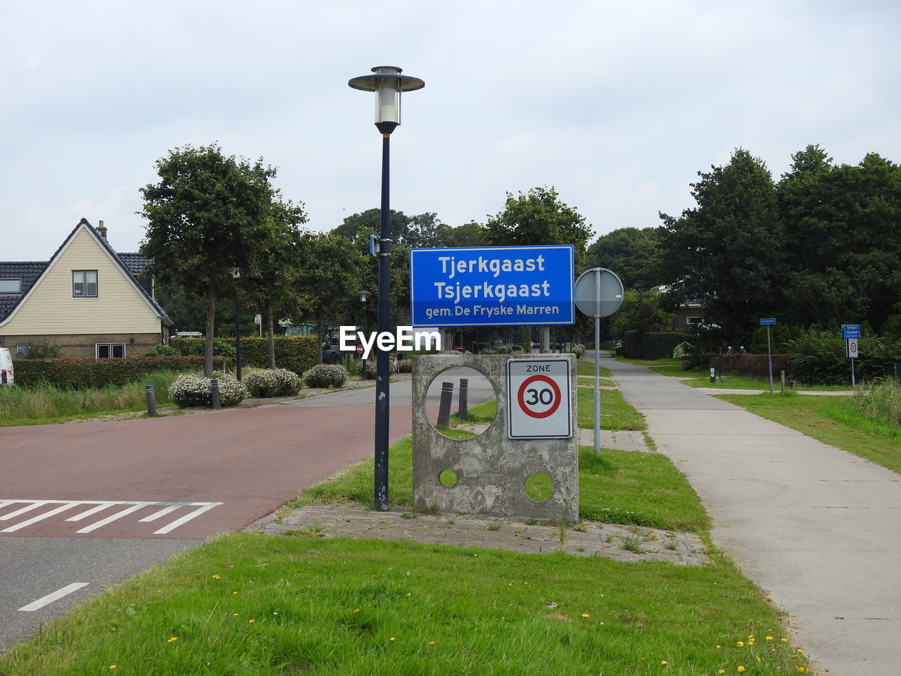 Road sign by trees against sky