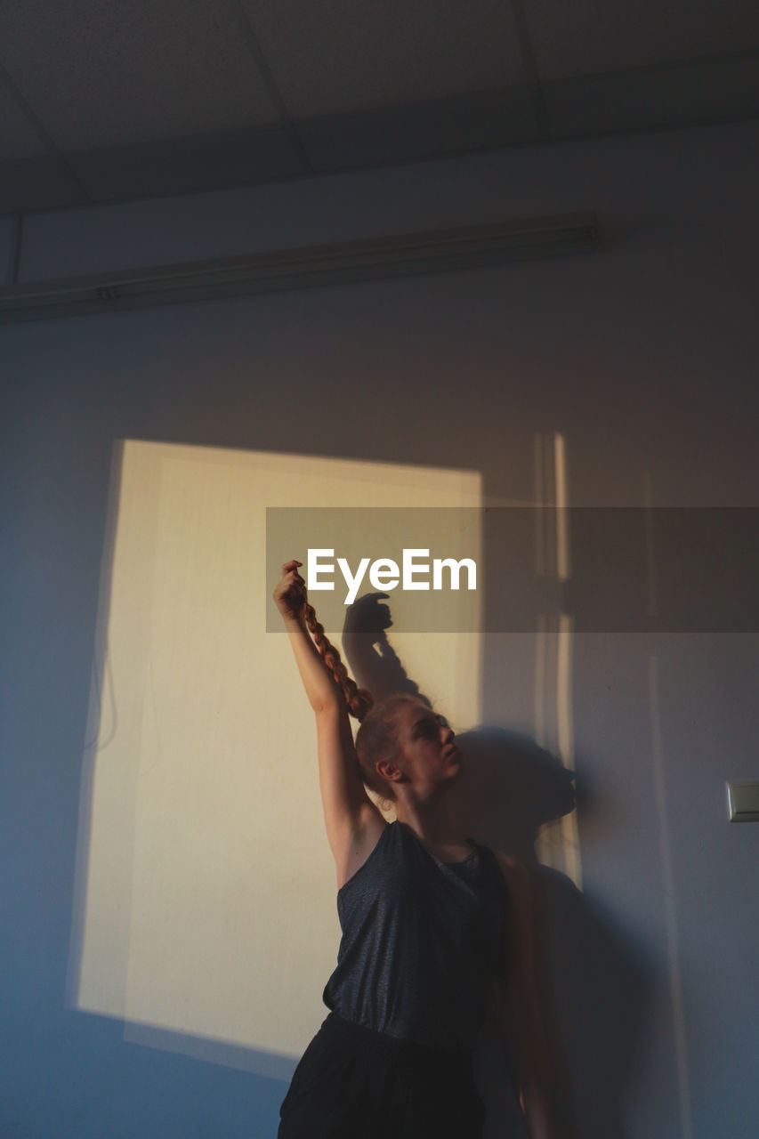 Woman with braided hair and hand raised standing against wall