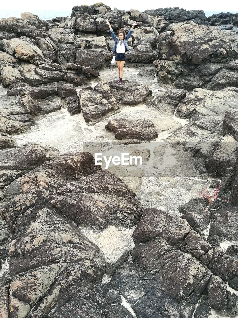 LOW SECTION OF WOMAN STANDING ON ROCK FORMATION BY SEA