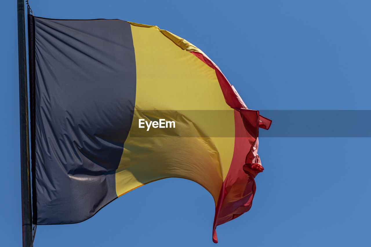 flag, wind, blue, environment, sky, patriotism, nature, red, clear sky, yellow, no people, red flag, low angle view, outdoors, sunny, day, textile, motion, emotion