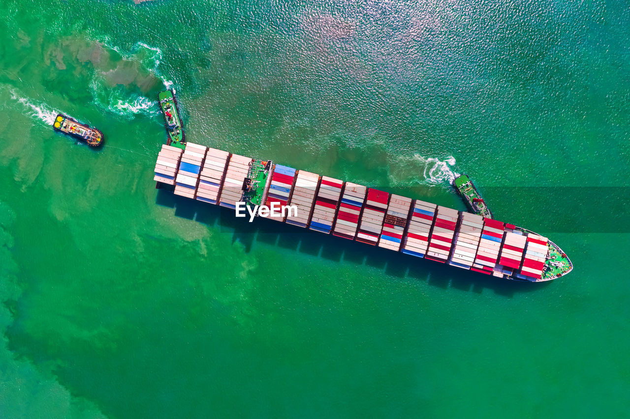 Aerial top view of ocean cargo ship with contrail in ocean ship carrying containers.