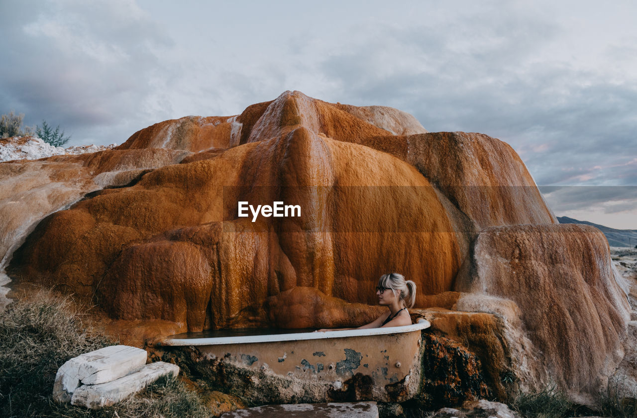 Woman sitting in bathtub at mystic hot springs during sunset