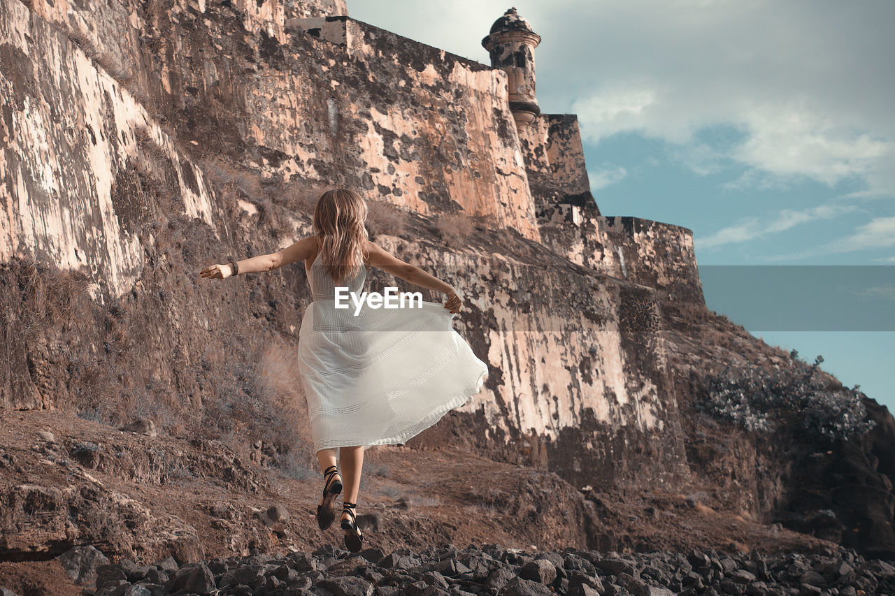 Rear view of woman standing on rock against fort