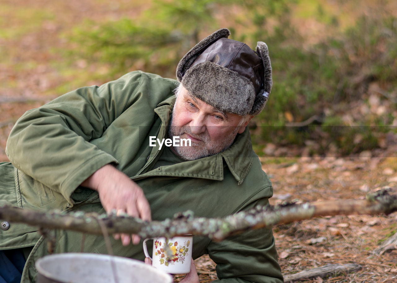 A forester in the forest drinks tea at rest, blurred forest background, bonfire with a pot over it