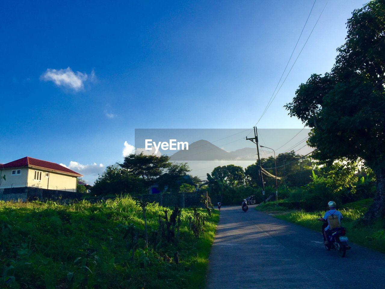 Rear view of man riding motor scooter on road by field against sky