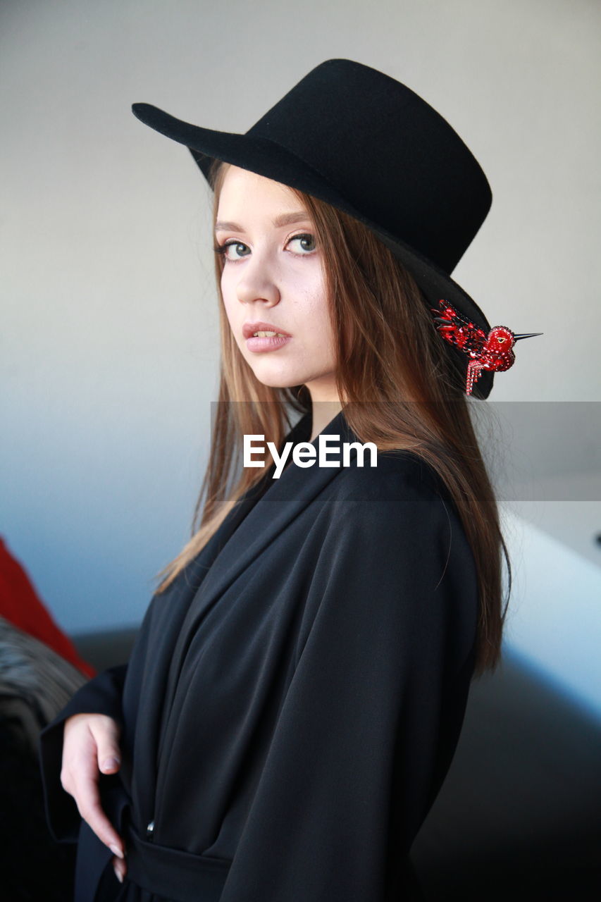 Portrait of beautiful woman wearing hat standing against wall