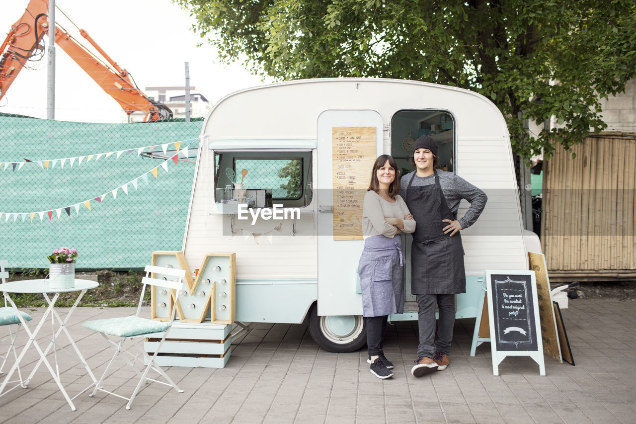 Full length portrait of confident owners standing outside food truck on street