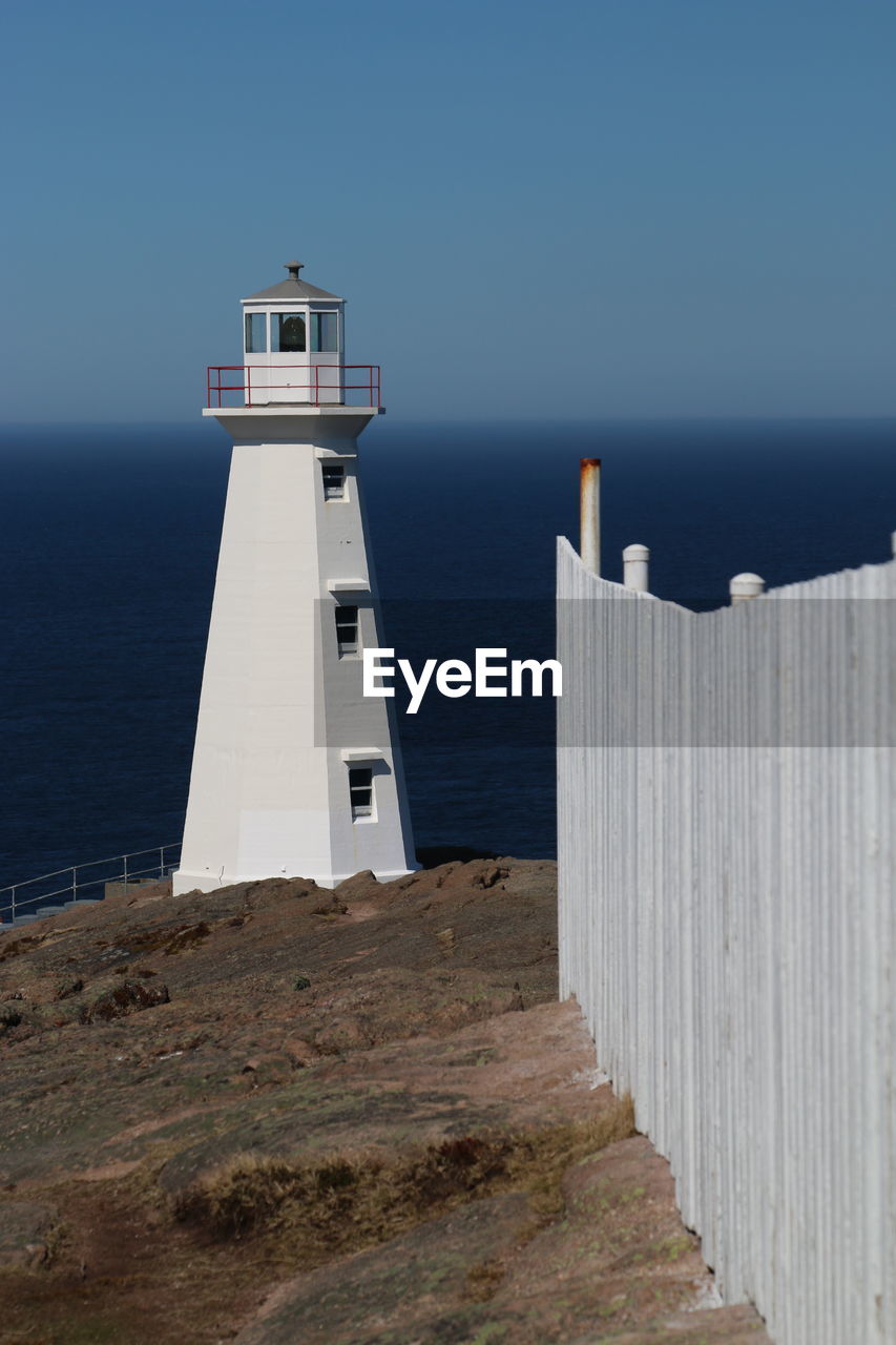 Lighthouse by sea against clear sky