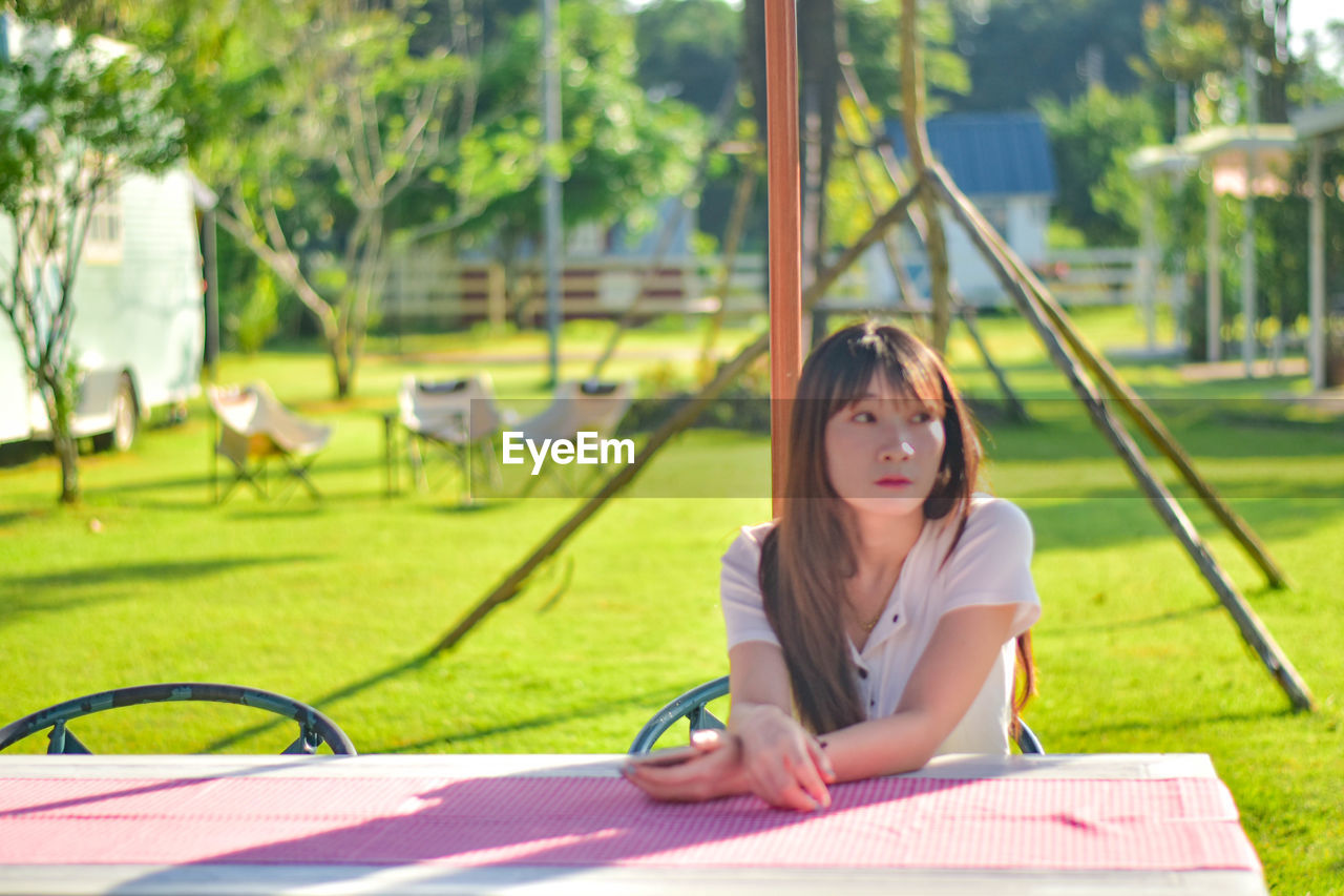 young woman reading book while sitting on swing in park