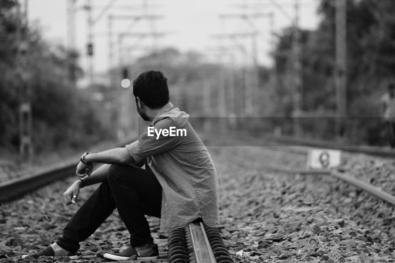 Side view of young man sitting on railroad track