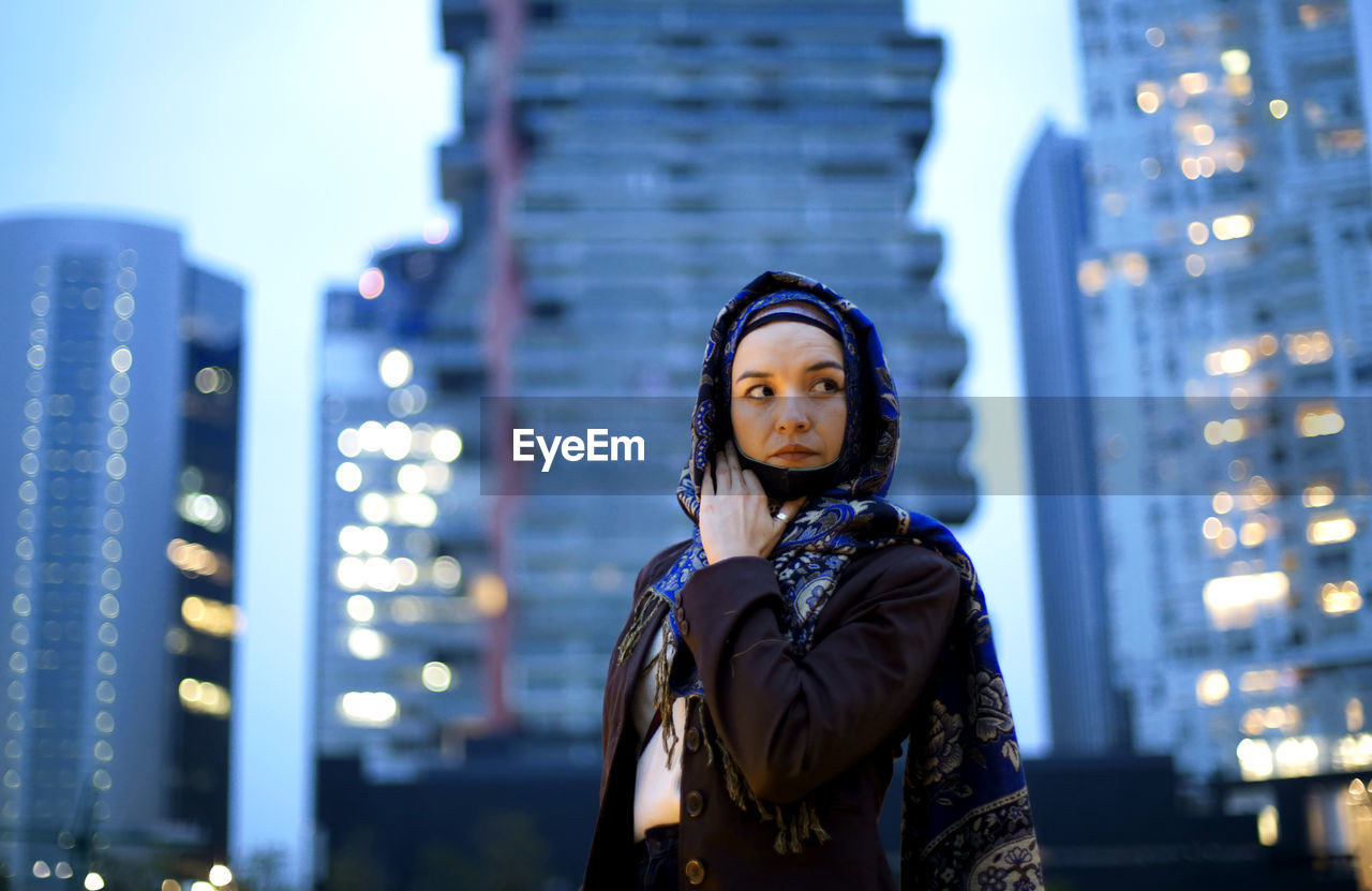 Portrait of young woman standing against illuminated city at night