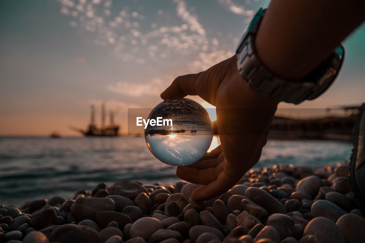 Close-up of hand holding crystal ball at beach during sunset