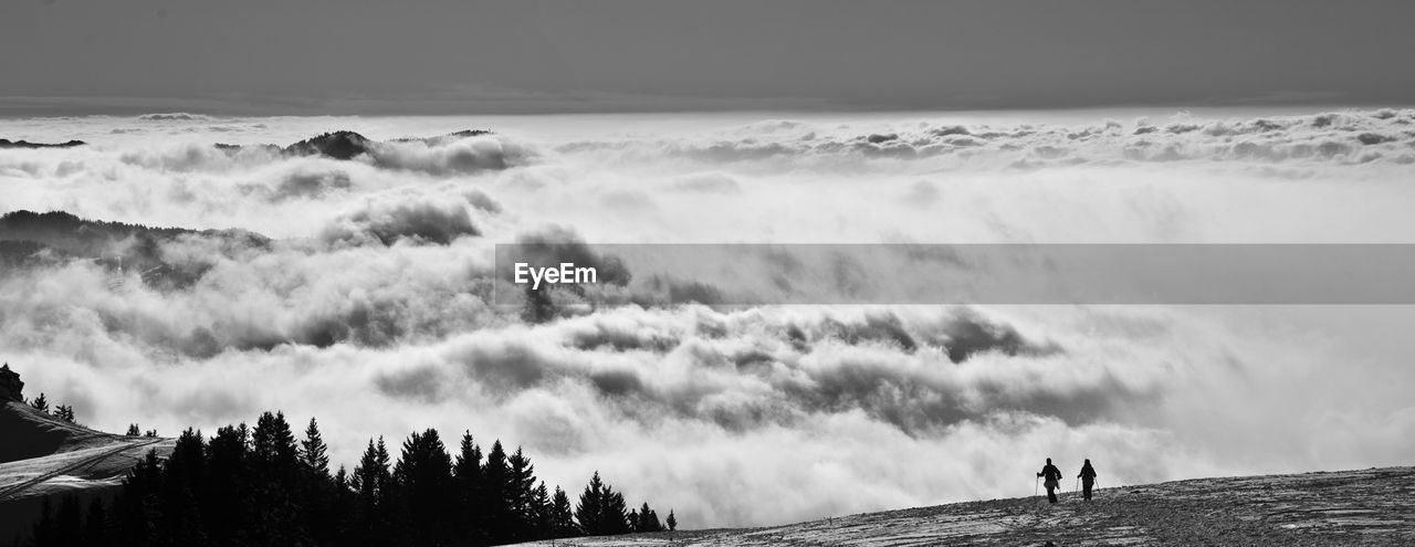 Silhouette people standing on mountain over cloudscape