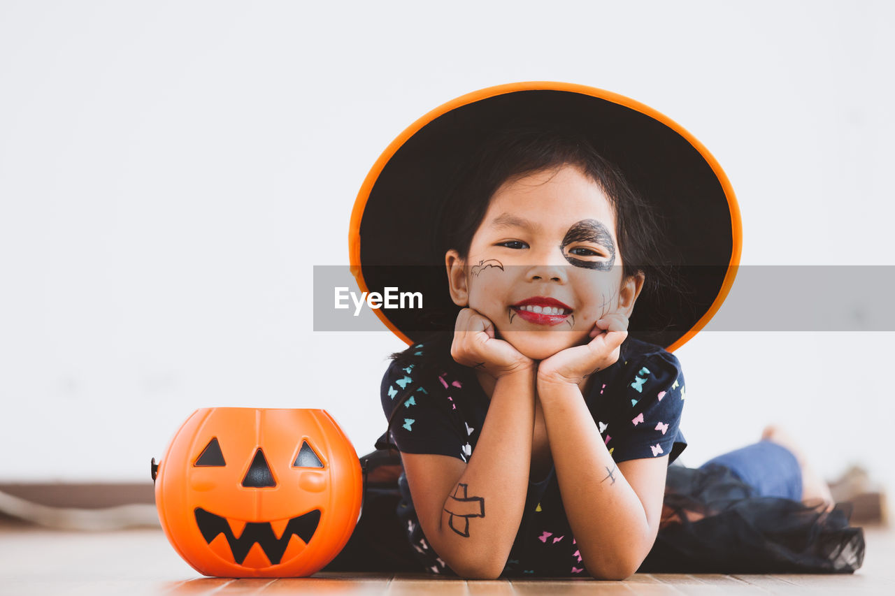 Portrait of cute playful girl with spooky make-up lying on floor at home during halloween