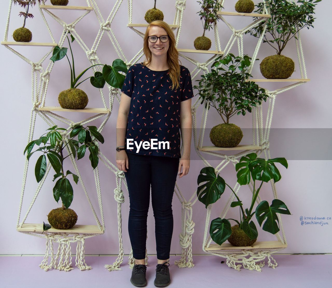 PORTRAIT OF SMILING YOUNG WOMAN STANDING AGAINST PLANTS