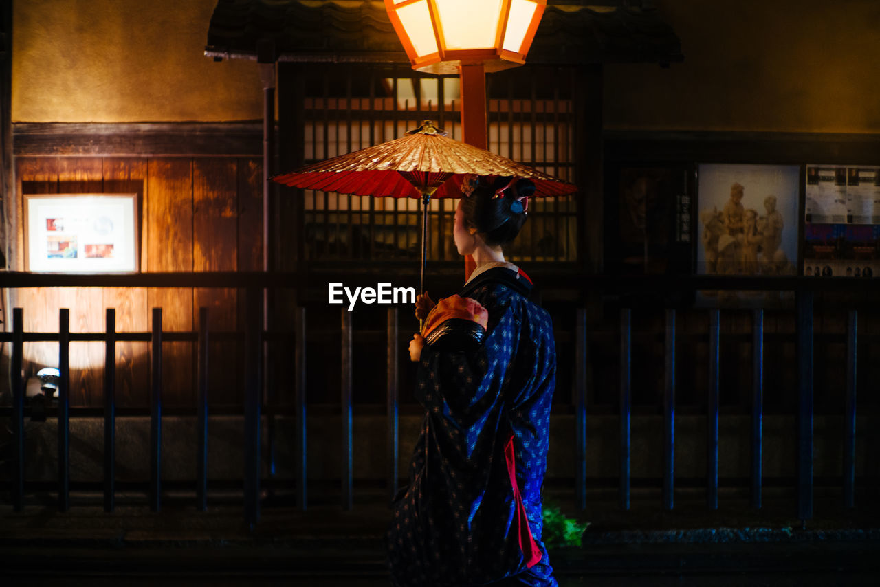 WOMAN STANDING AGAINST ILLUMINATED BUILDING AT NIGHT