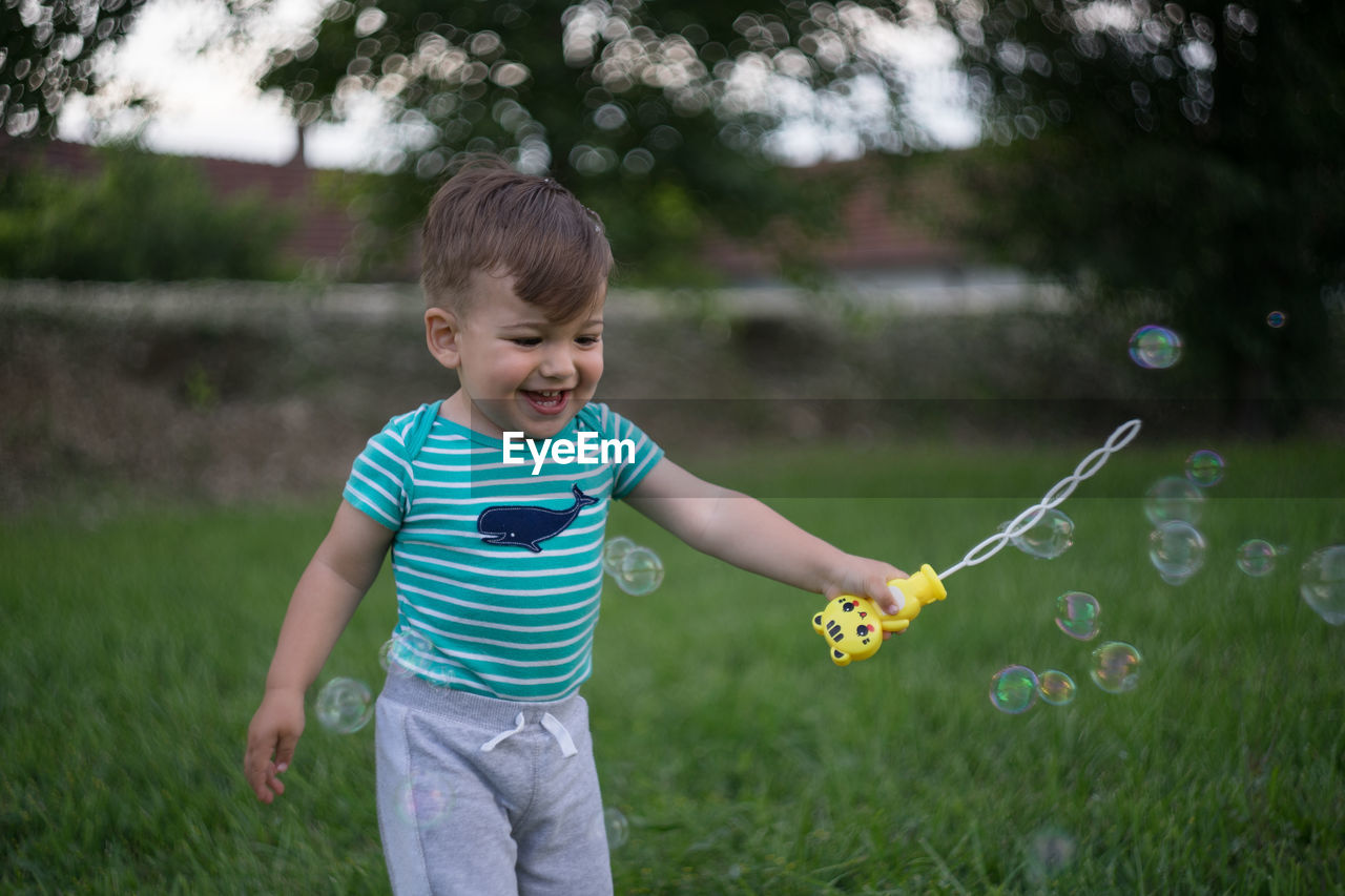 Cute boy playing with bubble wand on field