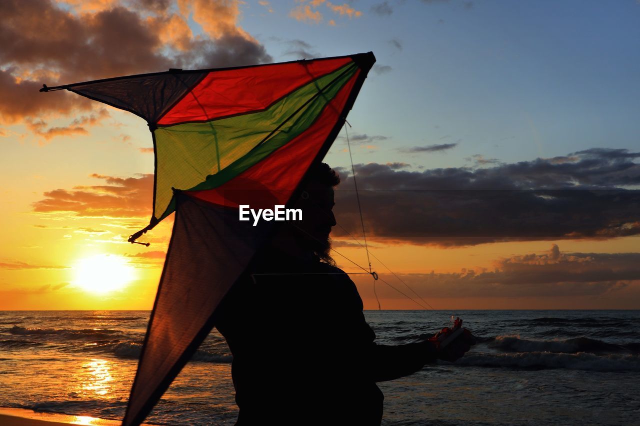 Silhouette of man holding kite while standing on beach