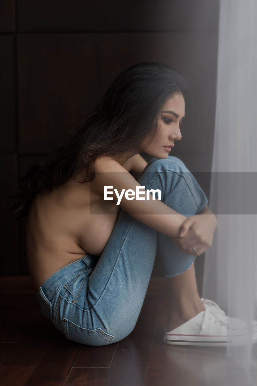 Shirtless woman sitting on floor at home