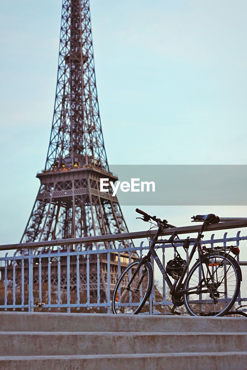 Bicycle by railing against eiffel tower