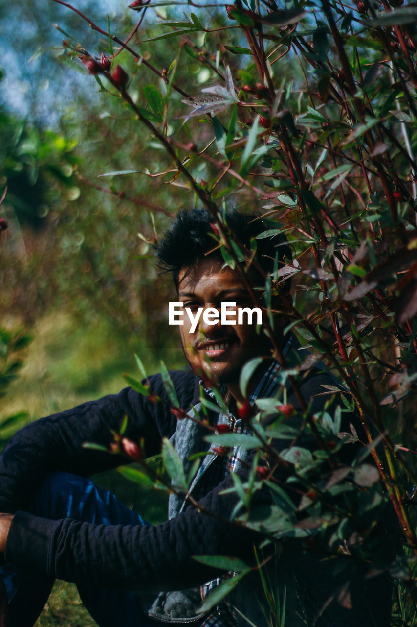 Portrait of young man sitting by plants in forest