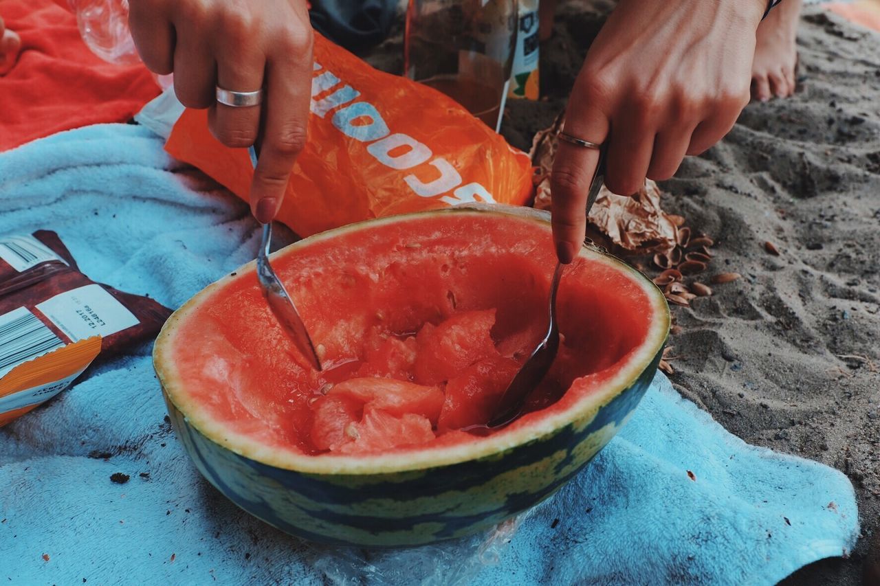 Cropped hands of woman eating watermelon at beach