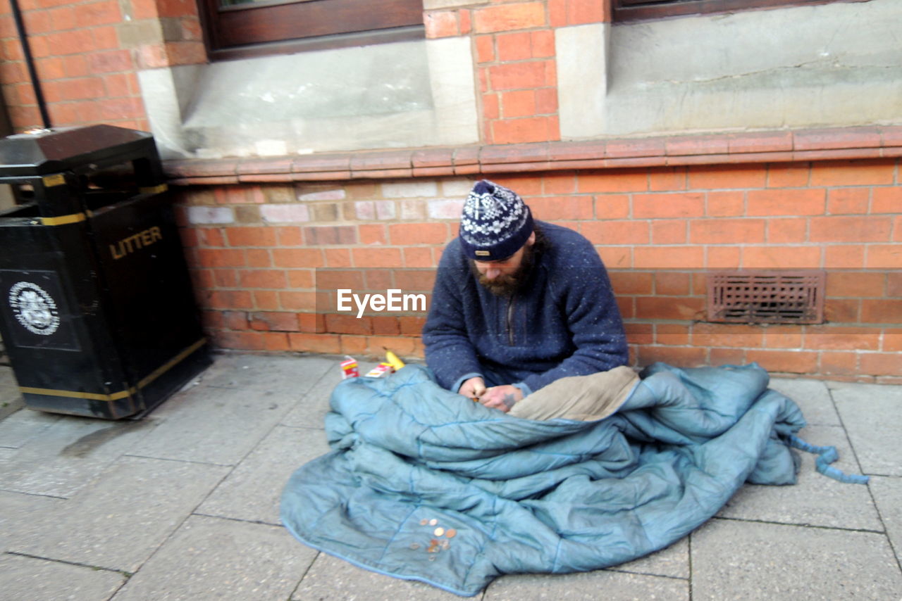 Beggar man with blanket sitting by building at footpath