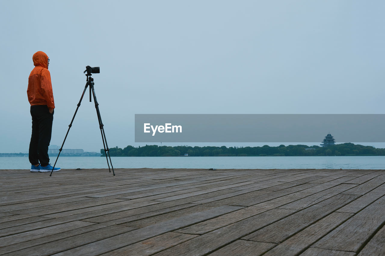 Man with tripod standing on pier over lake