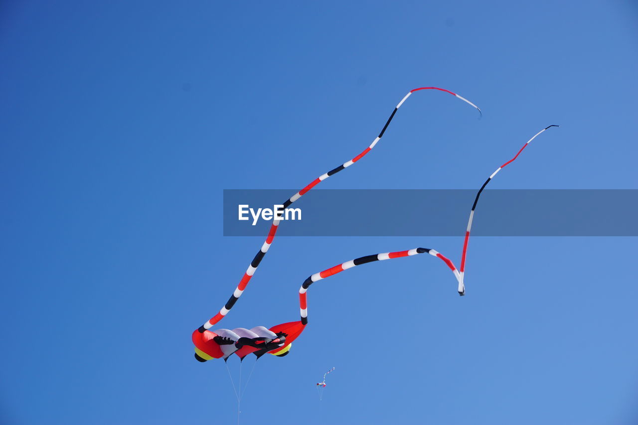 Low angle view of kites flying against clear blue sky