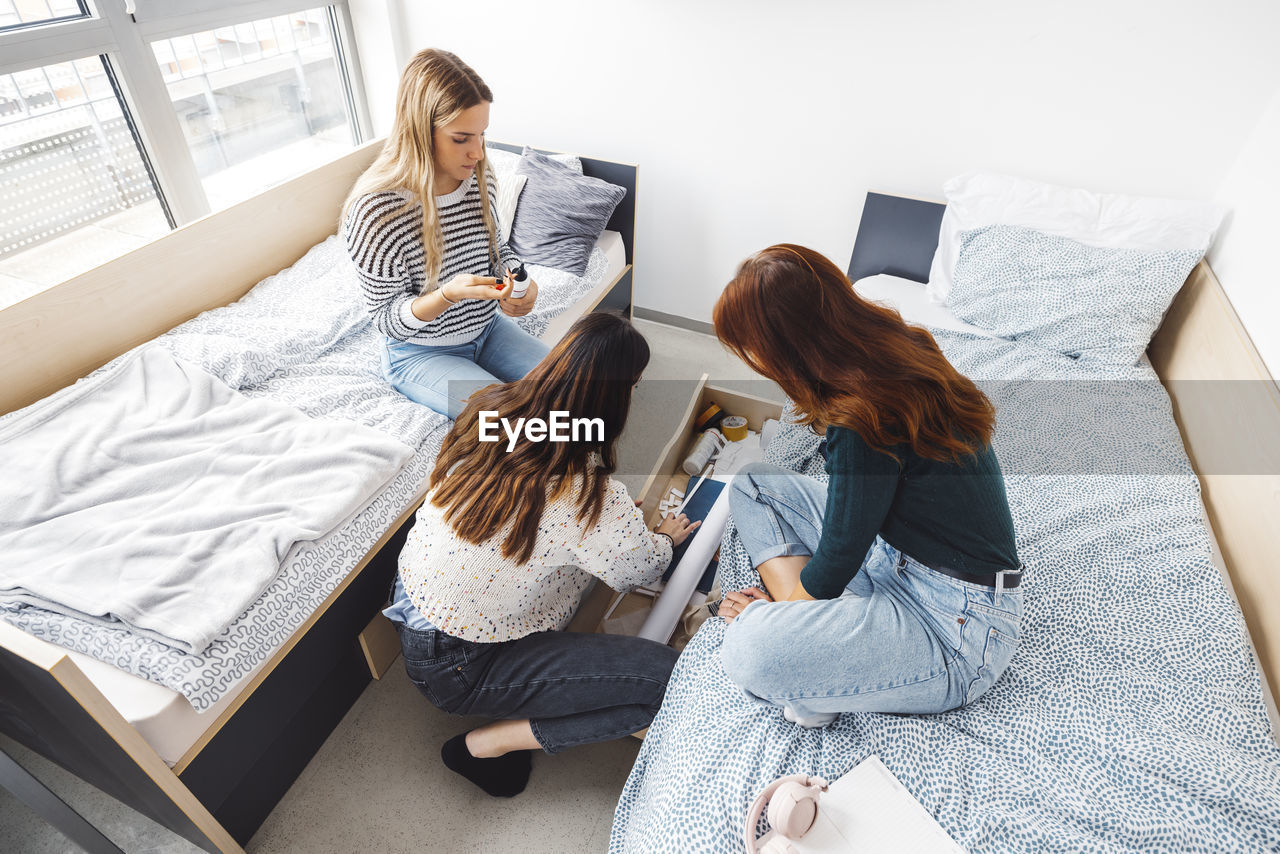 rear view of woman using digital tablet while sitting on bed at home