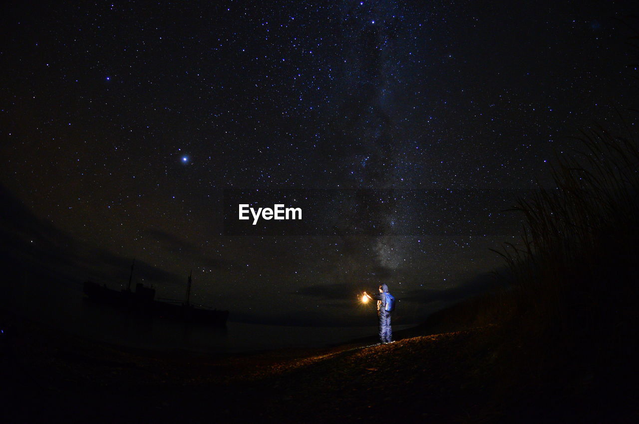 Man with lantern on field against sky at night