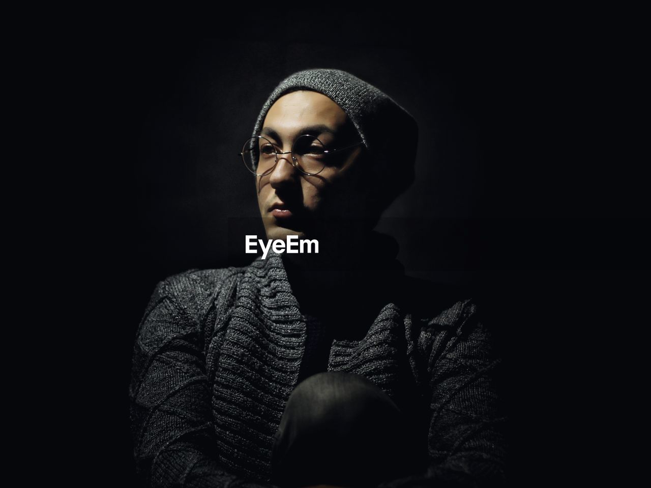 Thoughtful young man wearing eyeglasses against black background