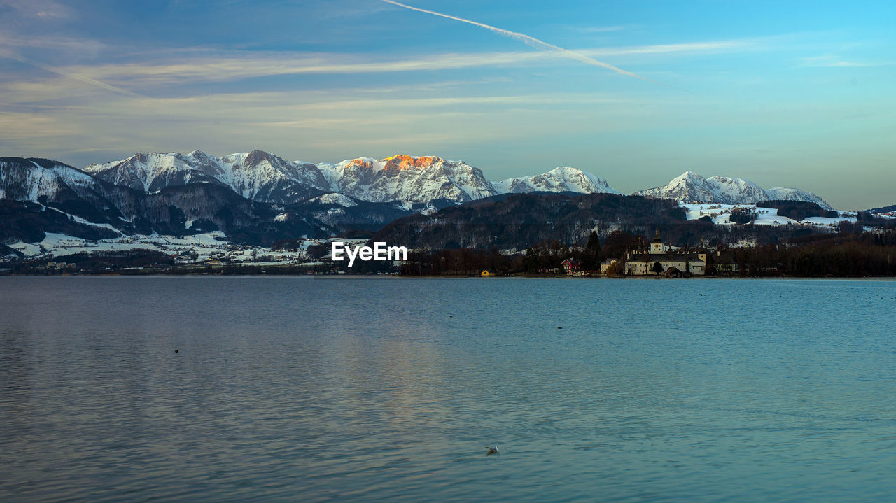 Scenic view of sea by snowcapped mountains against sky