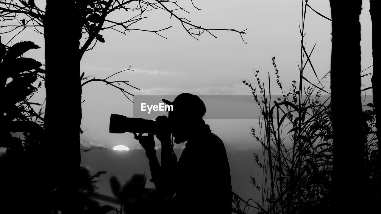 Silhouette man photographing against sky