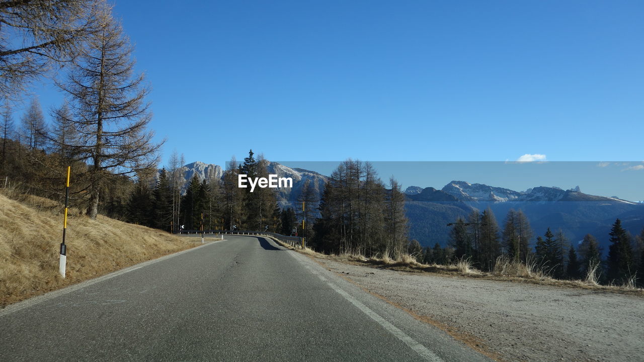 Road amidst trees against clear blue sky