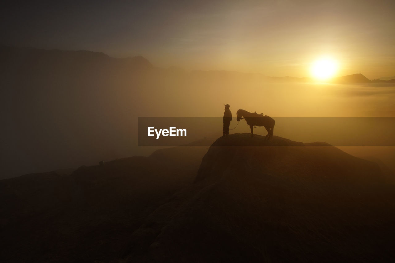 Silhouette man and horse on mountain cliff