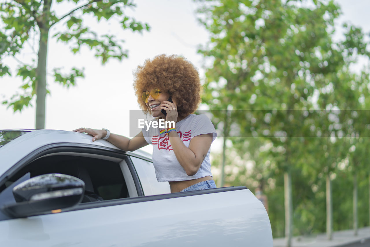 Woman with afro hair talking on the phone next to her white car